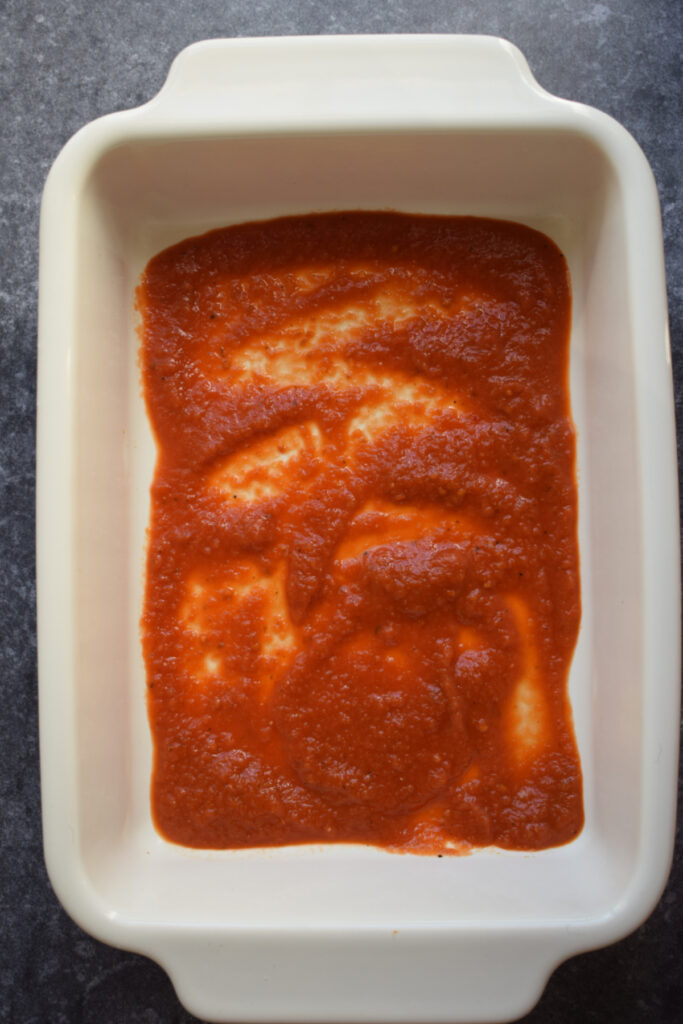 Marinara sauce in the bottom of a baking dish.