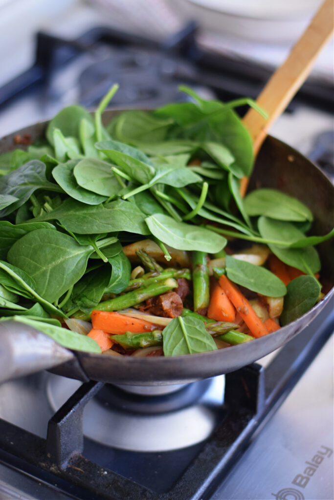 Adding spinach to vegetables in a wok.