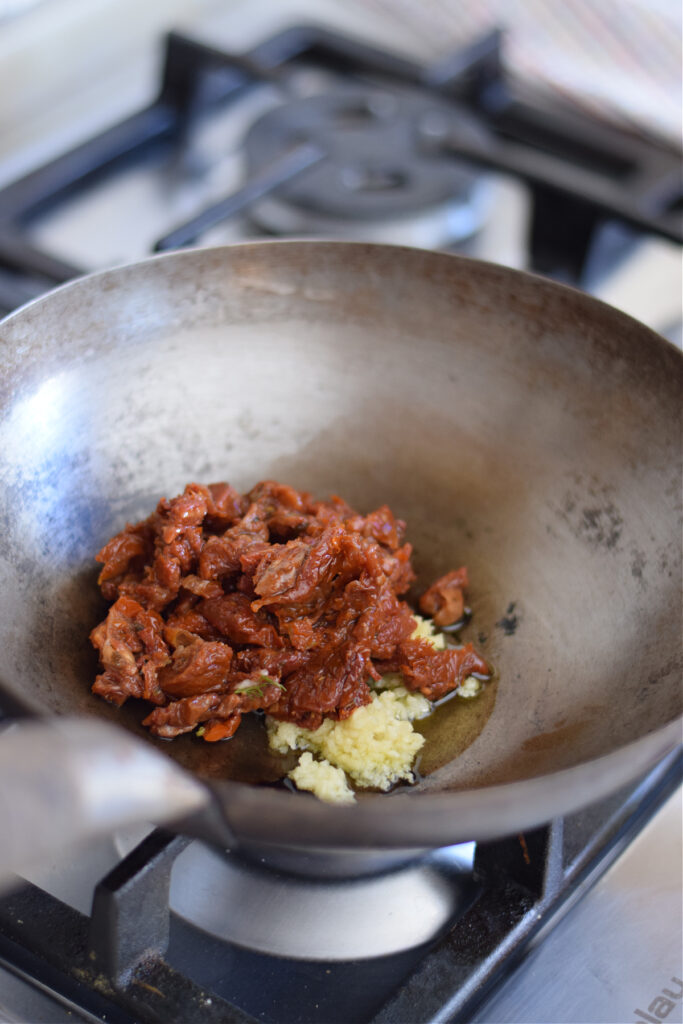 Adding sun dried tomatoes and garlic to a wok.