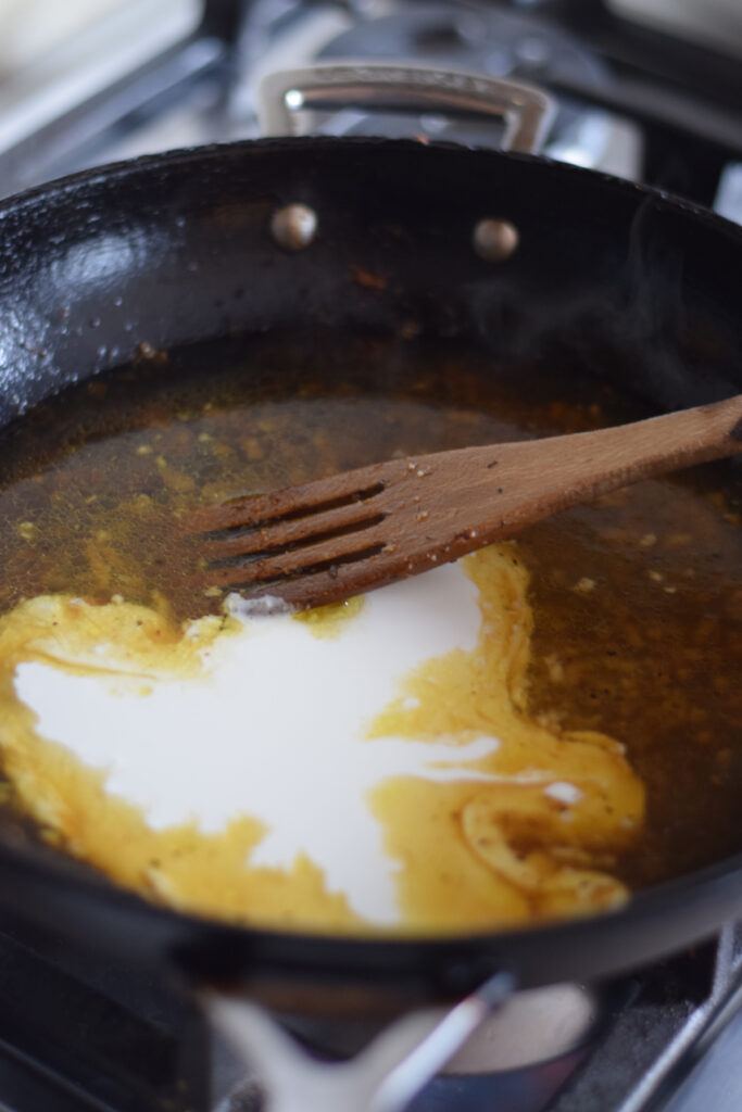 Adding cooking cream to a skillet with chicken broth.