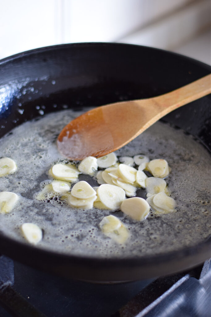 Cooking garlic slices in a skillet.