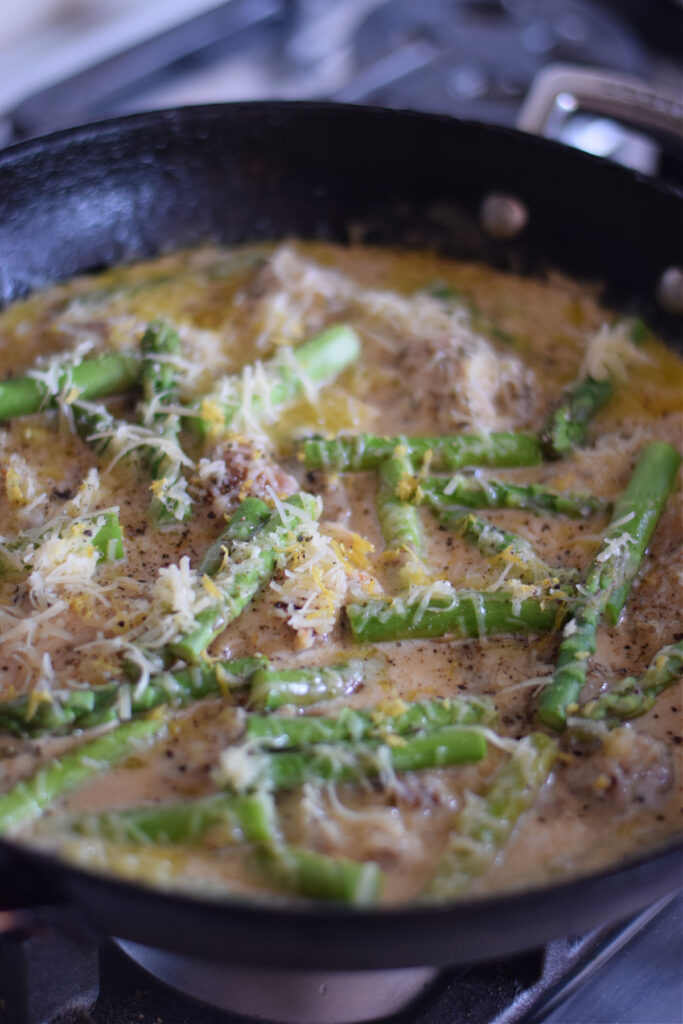 A dish with lemon cream chicken and fresh asparagus pieces.