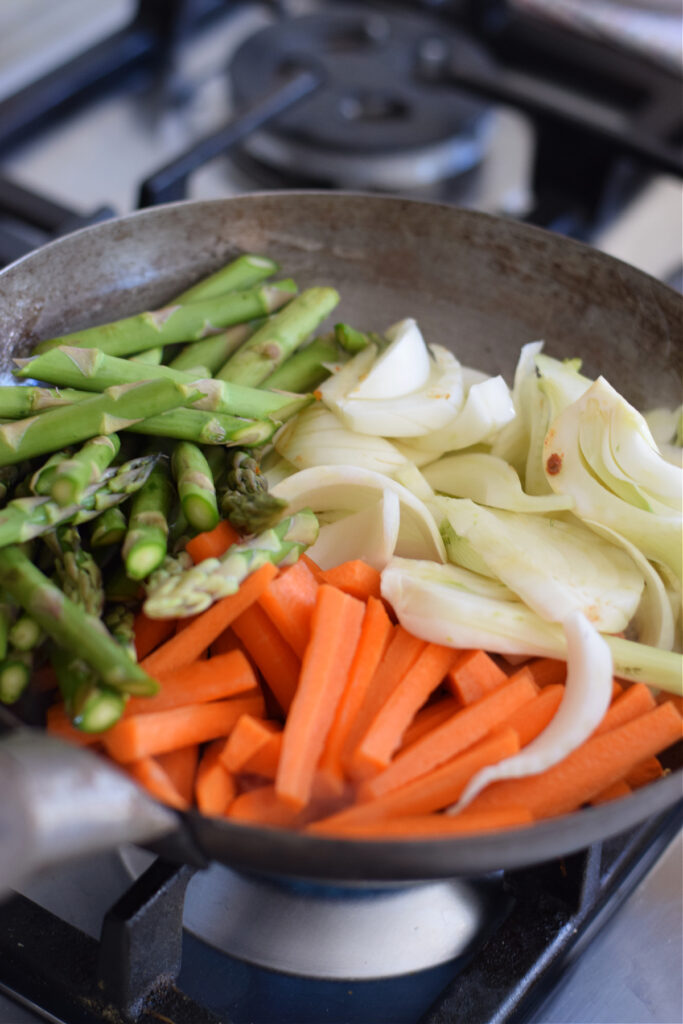 Adding carrots, asparagus and fennel to a wok.