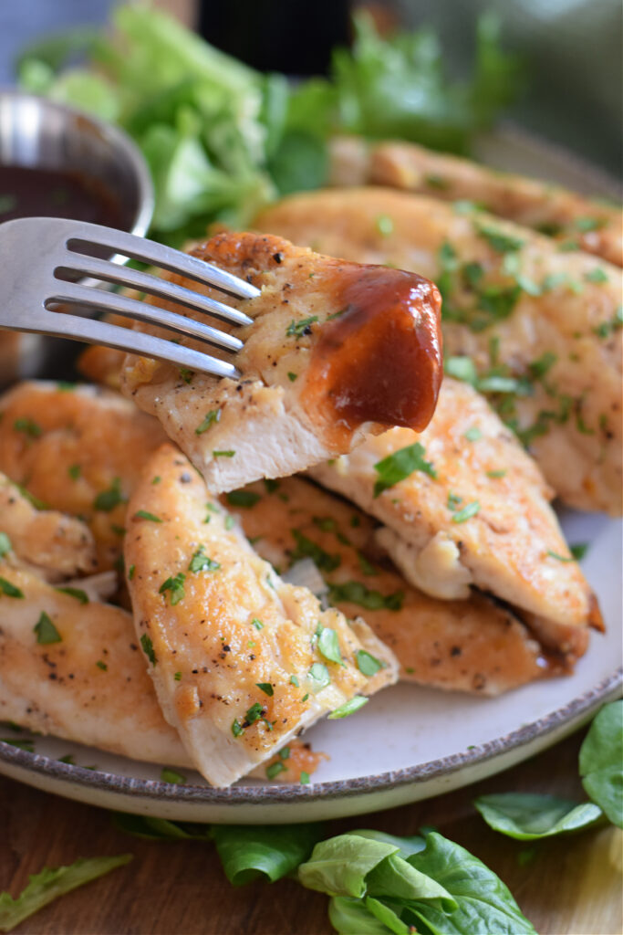 Close up of chicken tenders on a plate with a fork.