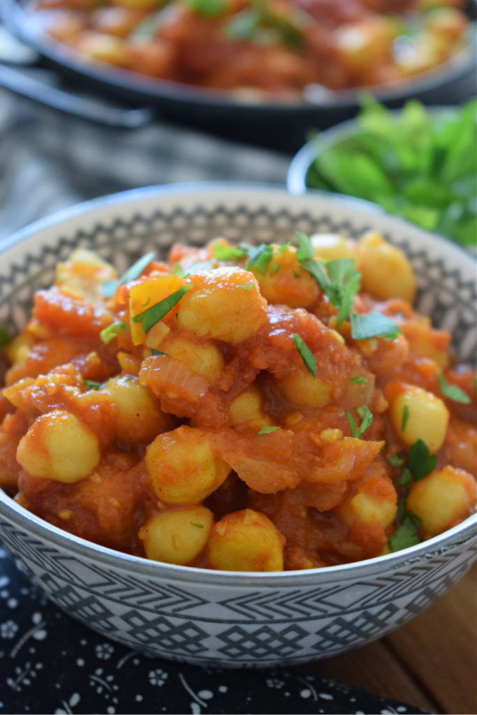 chickpea curry in a bowl wiht herbs in the background