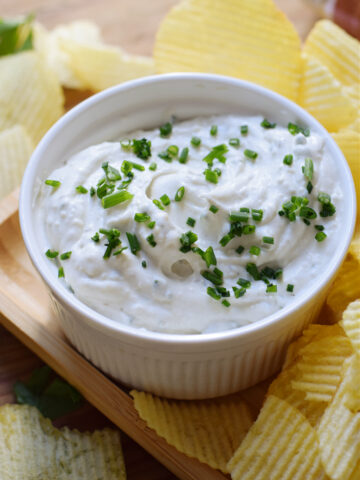 Dip with chives in a white bowl with chips on the side.