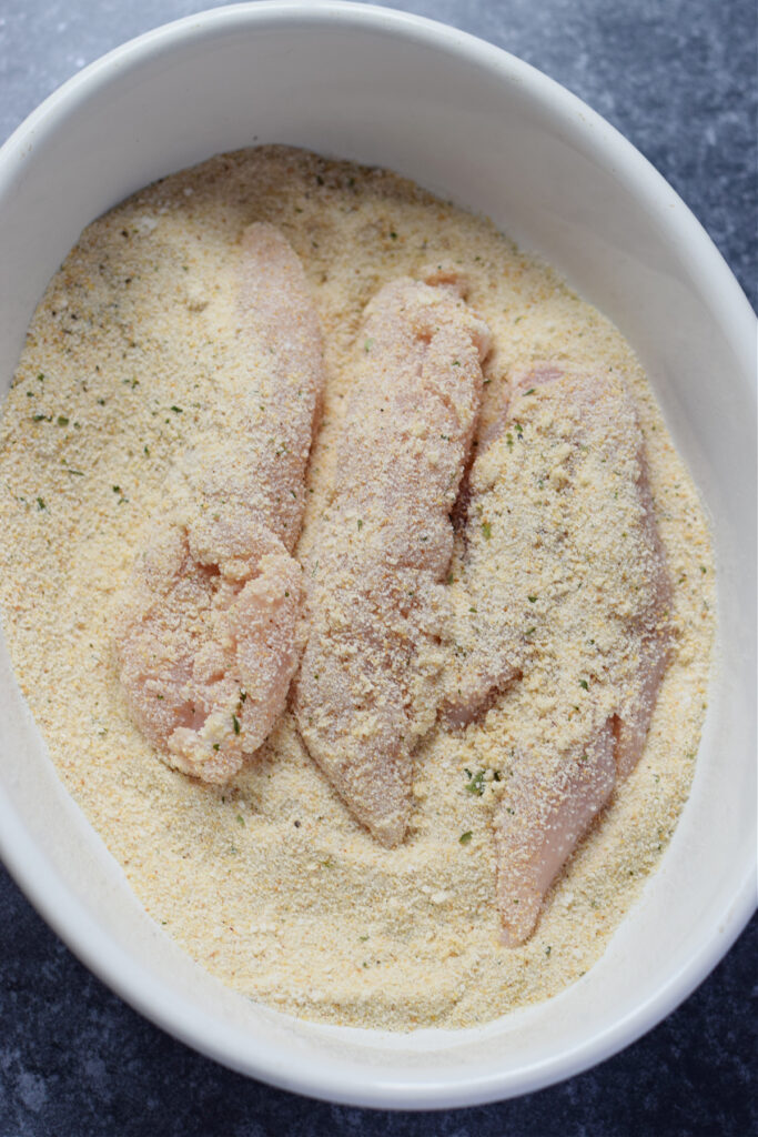 Coating chicken tenders in bread crumbs.