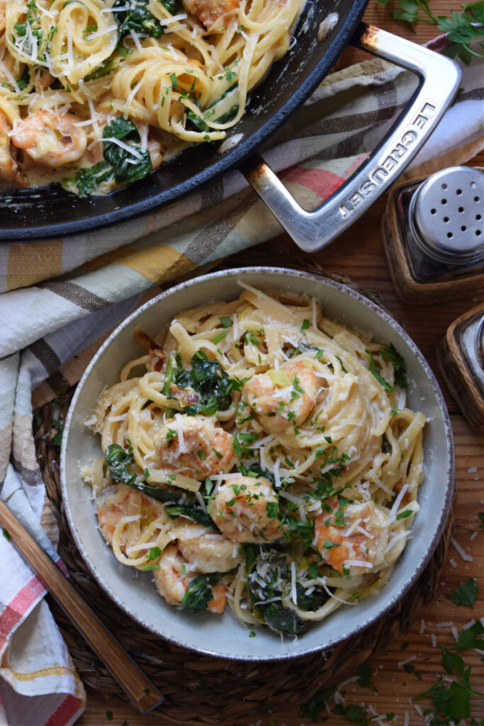 Pasta with shrimp and spinach in a bowl on a table.