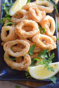 Crispy fried calamari rings on a black plate.