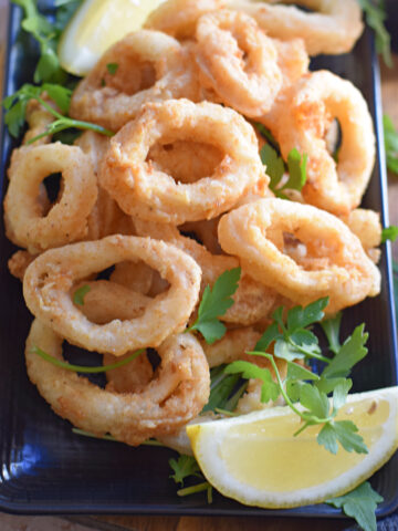 Crispy fried calamari rings on a black plate.