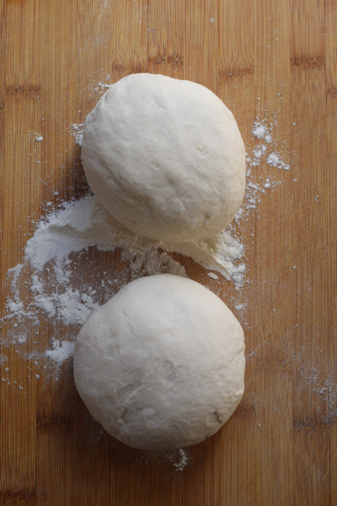 Two dough balls on a wooden board.