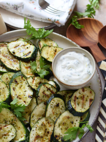 Marinated grilled zucchini on a plate with a dip.