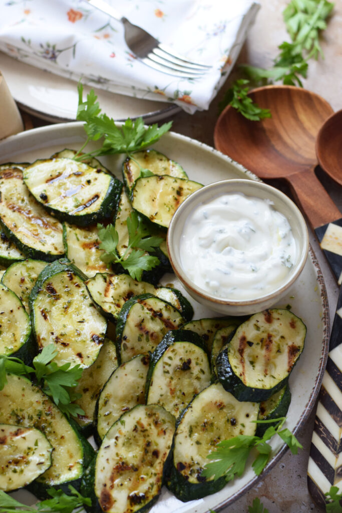 Marinated grilled zucchini on a plate with a dip.