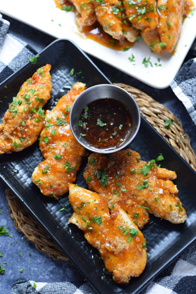 Honey garlic chicken tenders on a black plate.