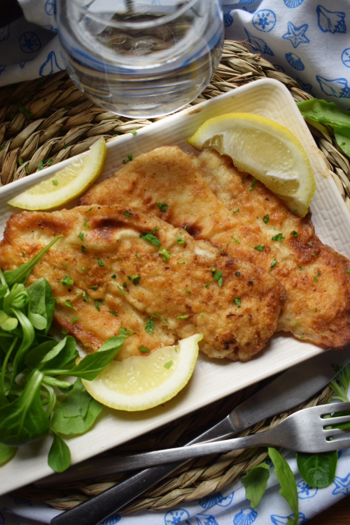 crispy pan fried hake on a plate with lemons and salad