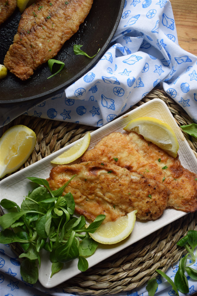 crispy pan fried hake with lemon wedges