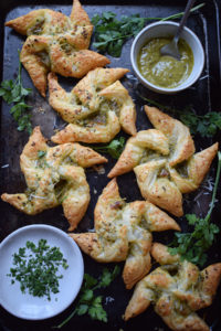 Pesto Puff Pastry Pinwheels on a baking tray with pesto and herbs