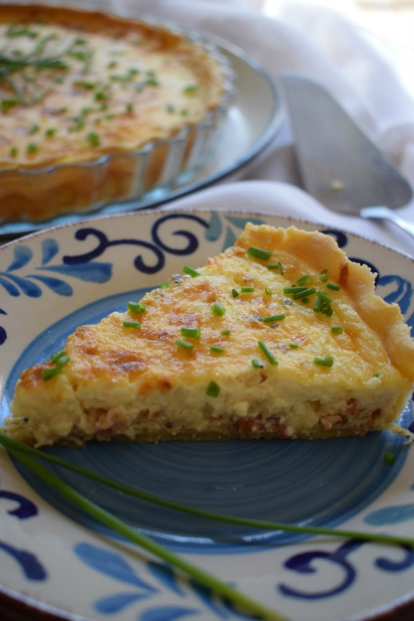 a slice of bacon and onion quiche on a plate with a quiche in the background