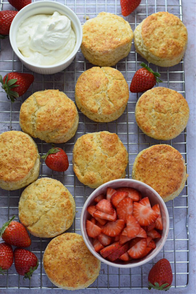Scones on a rack with whipping cream and strawberries.