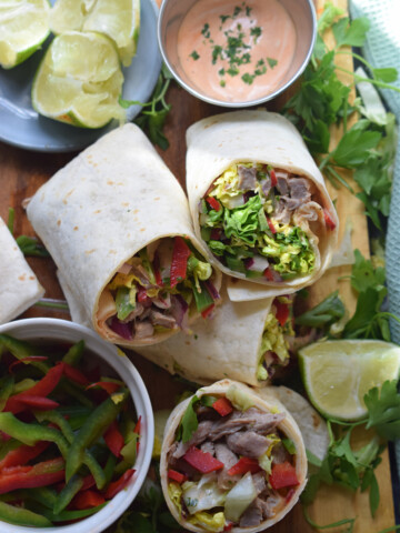 Beef salad wraps on a board with sauce and lime wedges.