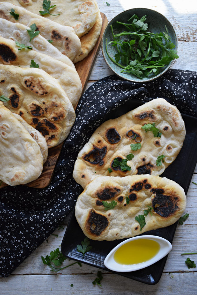 over head view of stove top nann bread on a white background with parsley and olive oil