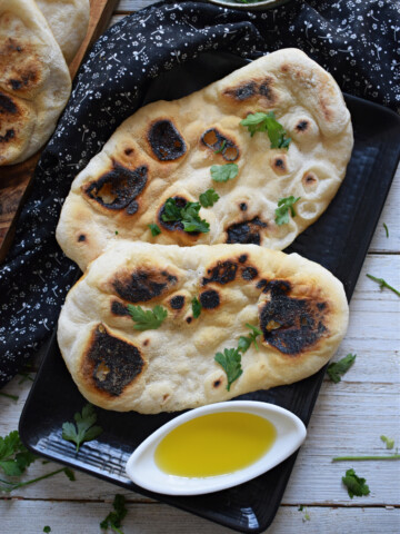 Stove top nann bread on a black plate with olive oil and parsley