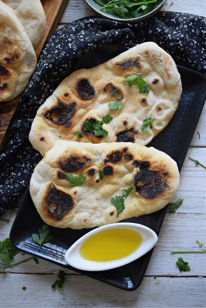 Stove top nann bread on a black plate with olive oil and parsley