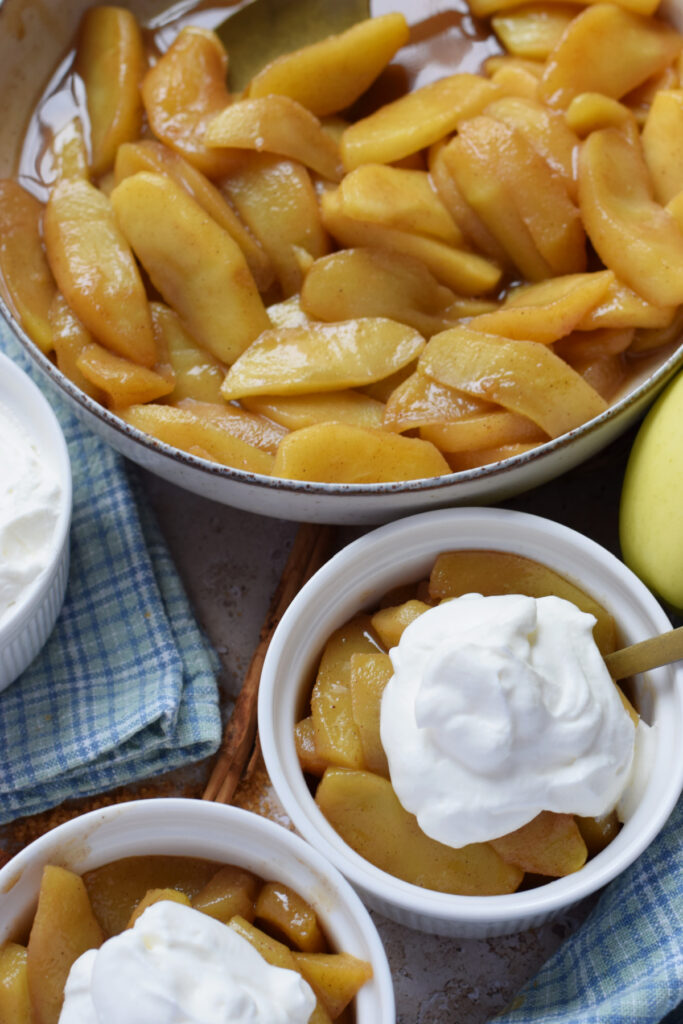 Caramelized apples in bowls with whipping cream.