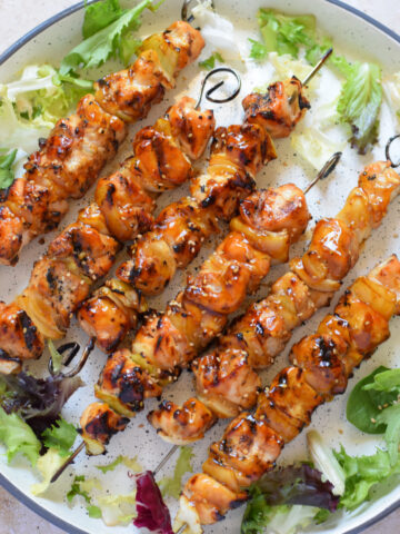 Chicken skewers on a white plate with lettuce.