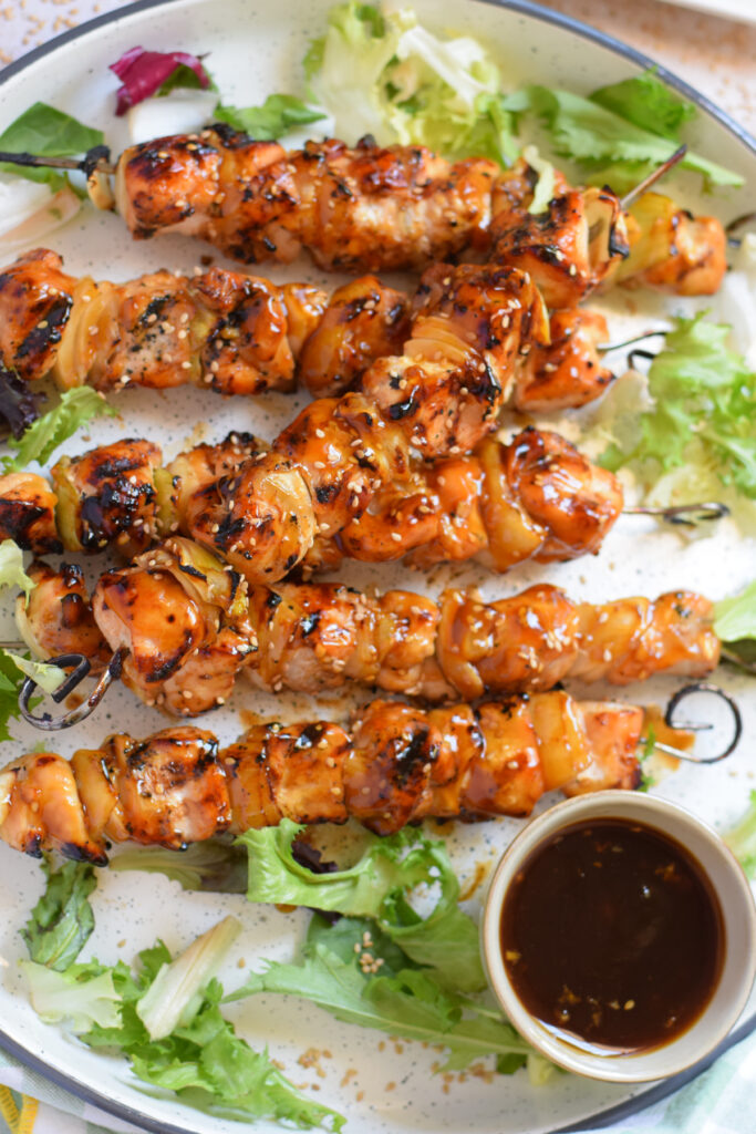 Teriyaki chicken skewers on a plate with lettuce and dipping sauce.
