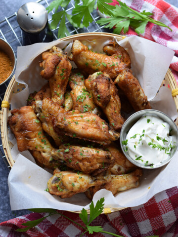 Chicken wings in a basket with a dip and a red tea towel.